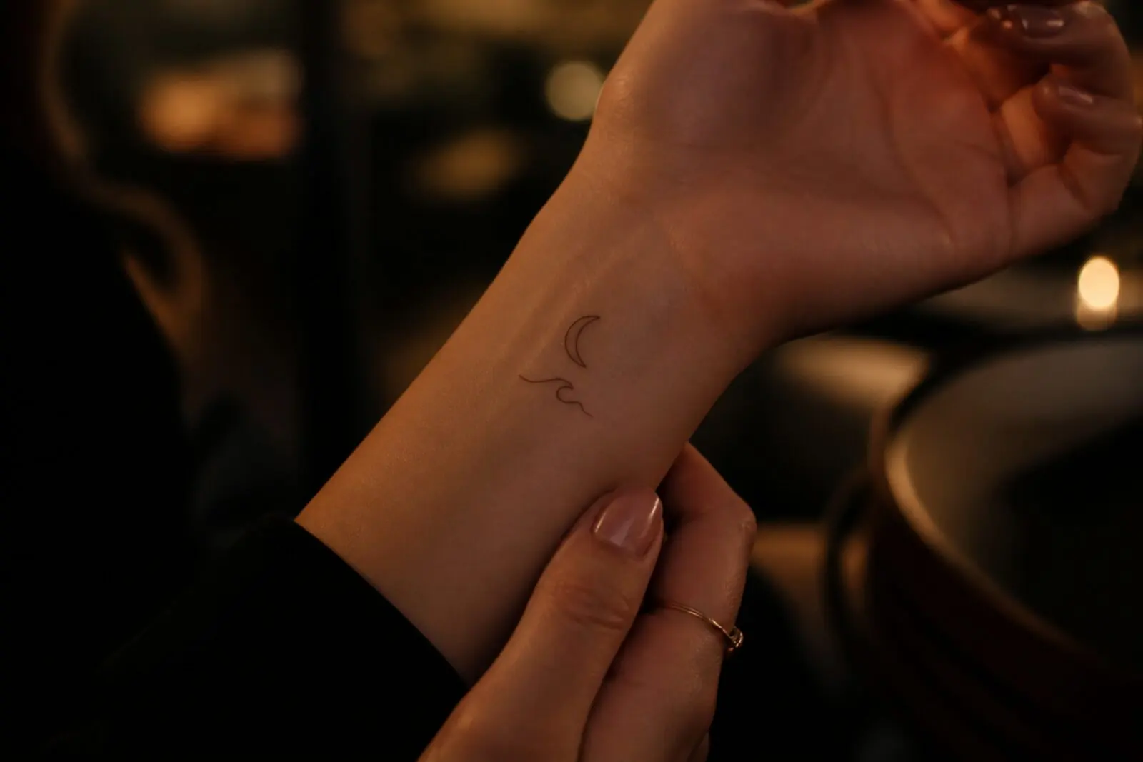 Fine line crescent and wave tattoo on a wrist — a discreet Istanbul souvenir