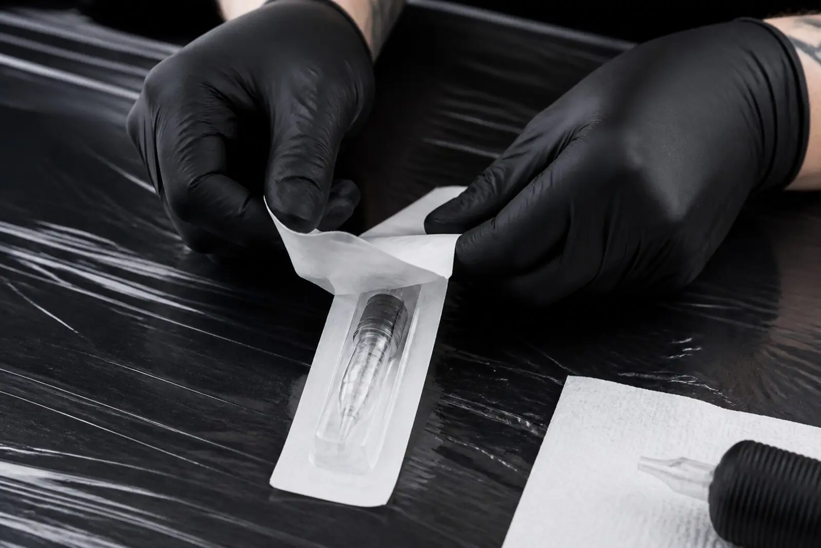 Gloved hands opening a sealed sterile tattoo needle cartridge package